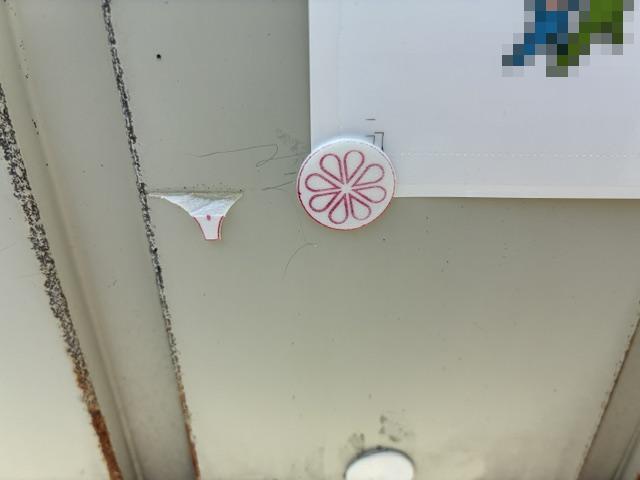 Circular pink sticker with a flower-like eight-petal design on a gray metal door.