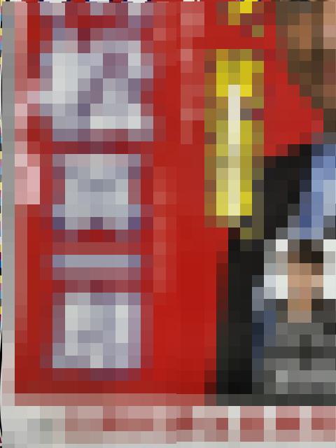 Person standing beside a tall red vending machine with white labels in a storefront setting.